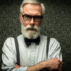 Mike, a 61-year-old writer. He's got a neat gray beard, long gray hair and he's wearing wire glasses, an office shirt with bow tie and the sleeve cuffs rolled up on his forearms.